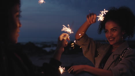 portrait of attractive mixed race sisters celebrating new years eve holding sparklers twins dancing on beach enjoying evening party