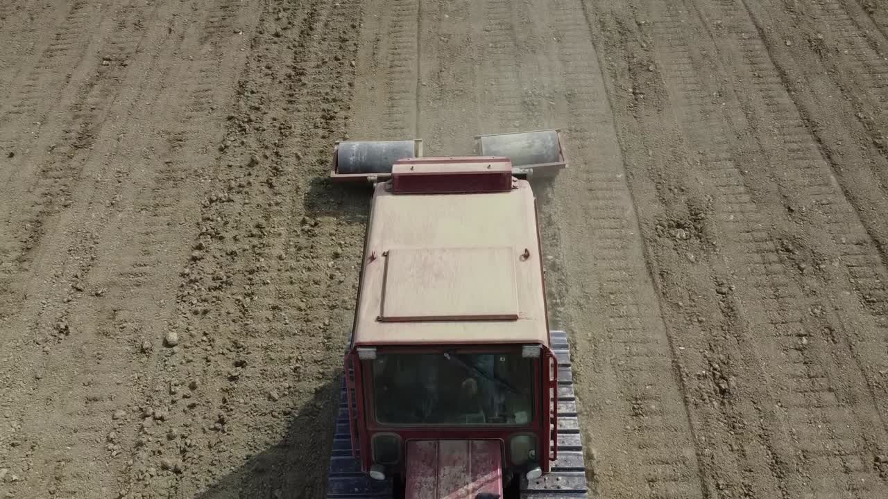 Drone fly above red tractor revealing triple roll system for soil preparation before seeding process in agricultural Italian farm