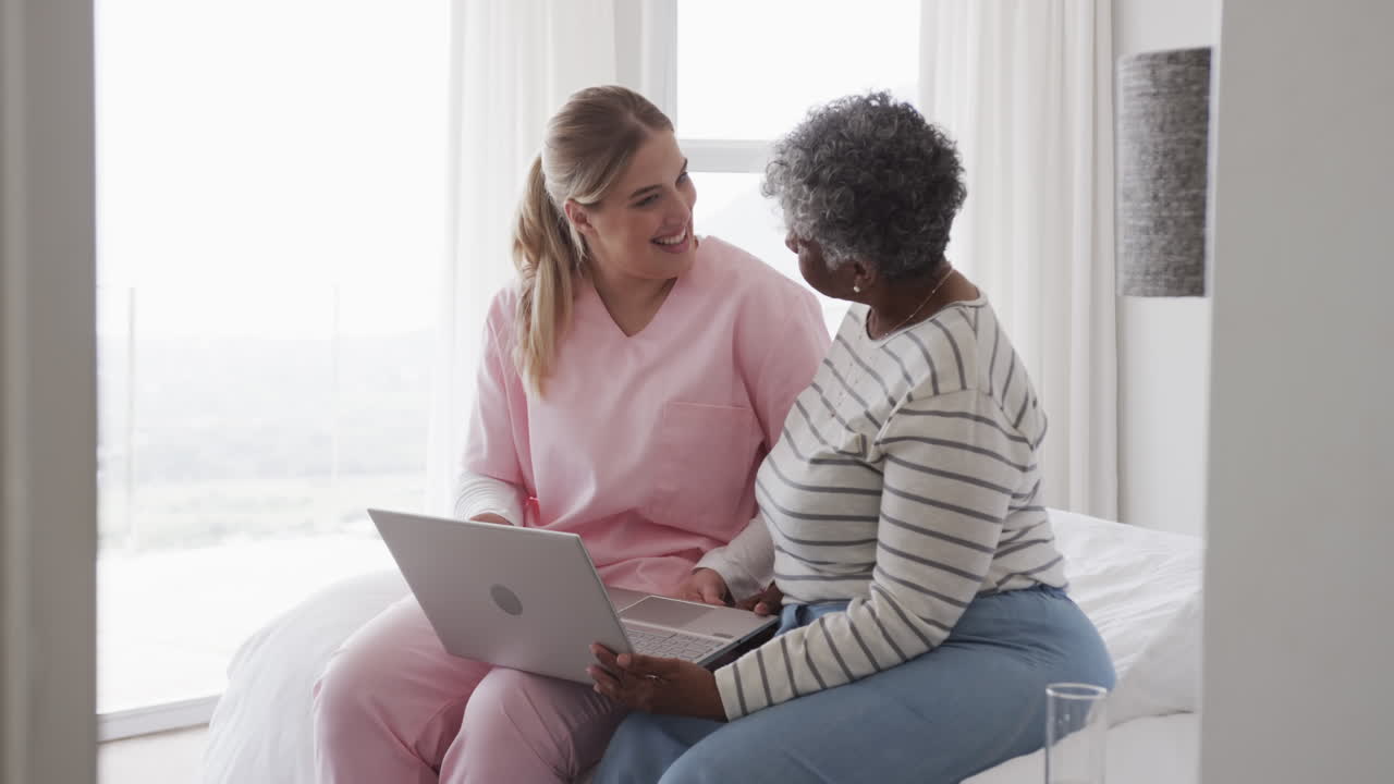 Caucasian female nurse and senior african american woman using laptop, copy space, slow motion