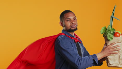 young adult acting as a superhero with a red cape presenting homegrown produce