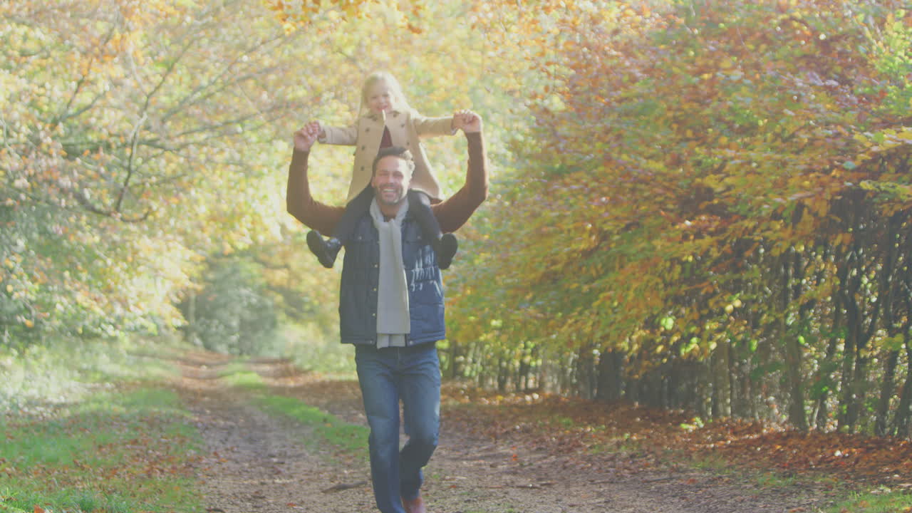 padre jugando a un juego cargando a su hija en los hombros en una caminata familiar a lo largo de la pista en el campo de otoño