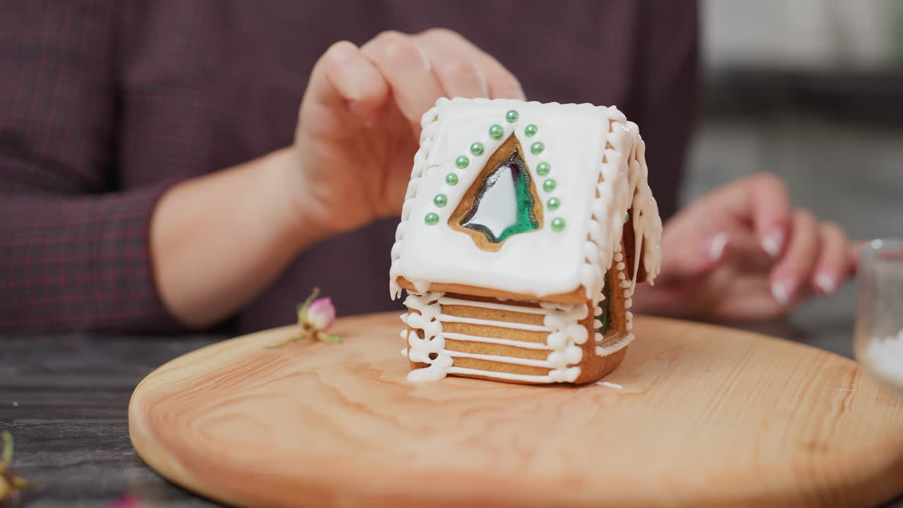 Nahaufnahme einer Person, die sorgfältig einen Kuchen mit Zuckerguss verziert, während ein Glasbehälter eine rote Kerze hält, mit festlicher Atmosphäre und verschwommenem Hintergrund der Küchenumgebung