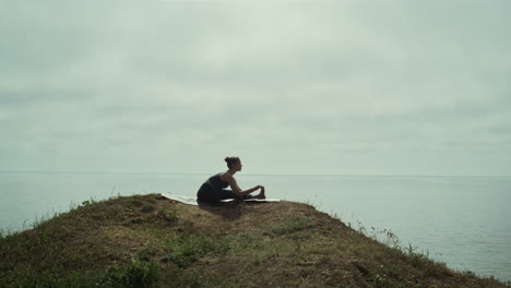 Frau-Workout-Yoga-Sitzend-Am-Grünen-Hügel-Am-Meer.-Silhouette-Eines-Jungen-Mädchens,-Das-Sich-Streckt