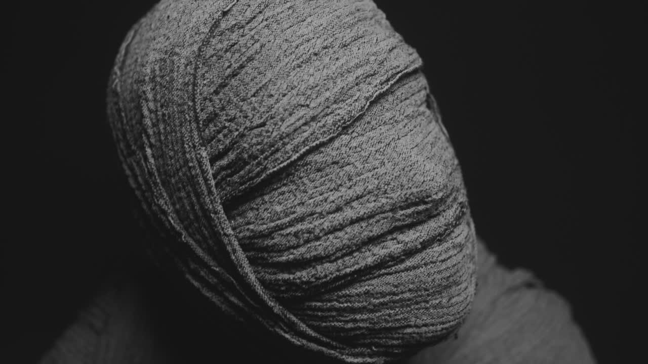 A mummy of a woman on a dark backdrop rises her head