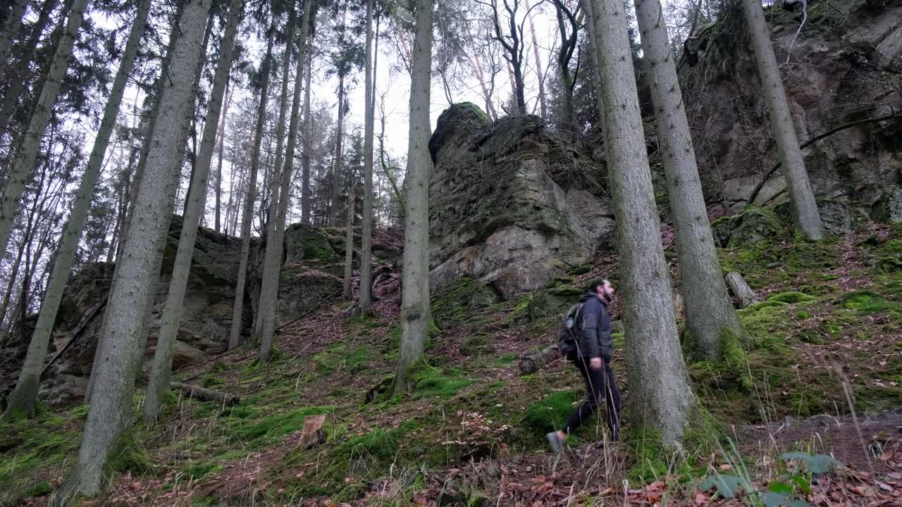 Man walking upwards near Huge Rock Formations in Mullerthal Hiking Trail in Luxembourg - Camera on side