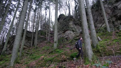 hombre caminando hacia arriba cerca de enormes formaciones rocosas en la ruta de senderismo mullerthal en luxemburgo - cámara a un lado