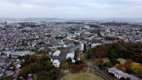 A-dense-cityscape-with-scattered-greenery-under-cloudy-skies,-hint-of-urban-sprawl,-aerial-view