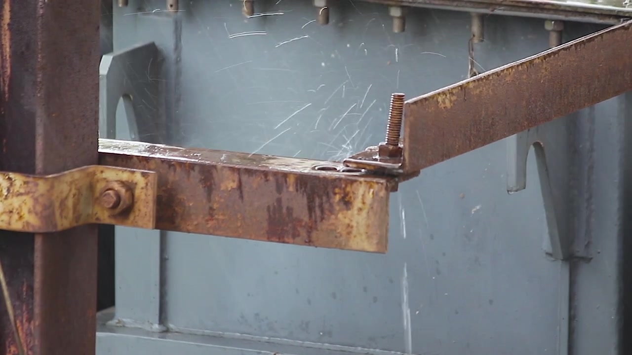 Rusted steel bracket with bolts on industrial machine housing, weathered metal texture close up, aged corroded hardware detail shot outdoors.