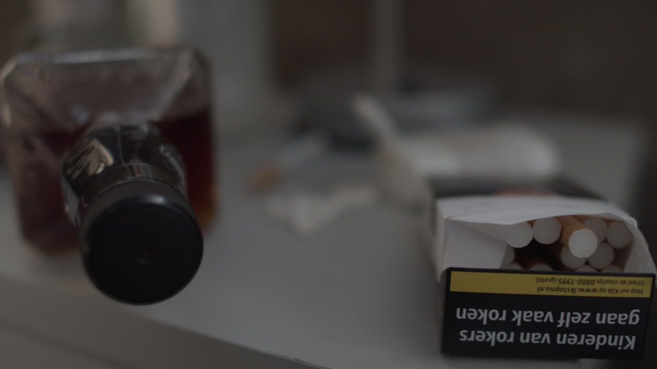 licor fuerte, pastillas y cenicero en una mesita de noche, de mano, cerca