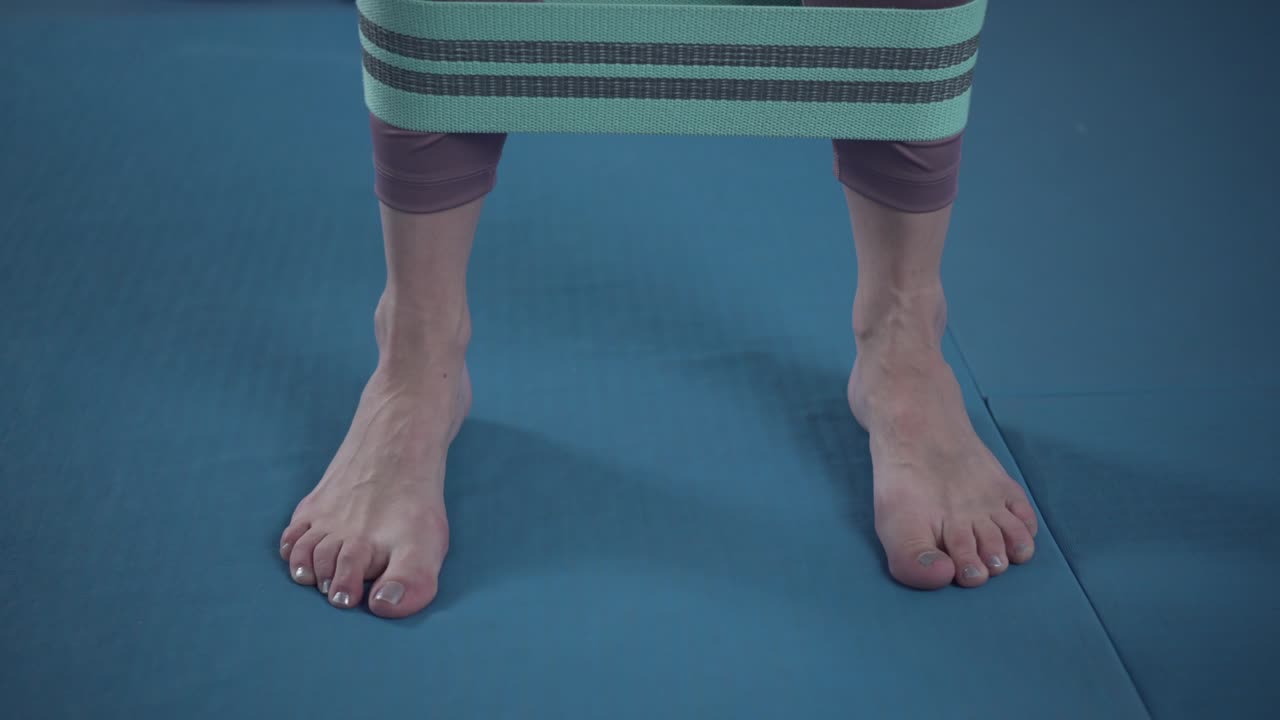 운동복을 입은 운동선수 여성은 발바닥으로 두꺼운 탄력적인 직물 운동밴드를 사용하여 스트레치 피트니스 부티 루프, 체육관 밴드, 웨이트 스트, 운동 근육을 사용합니다.