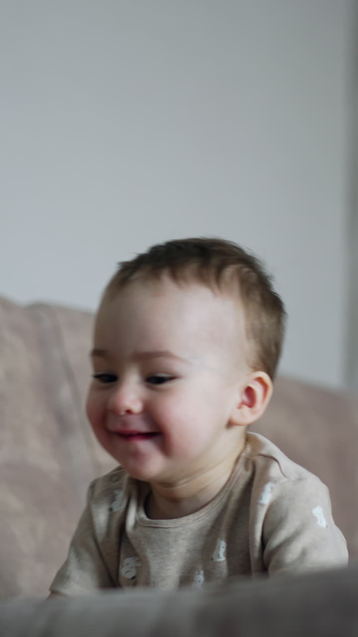 Active little kid jumps happily on the sofa. Adorable baby boy plays with his mommy at home. Vertical video