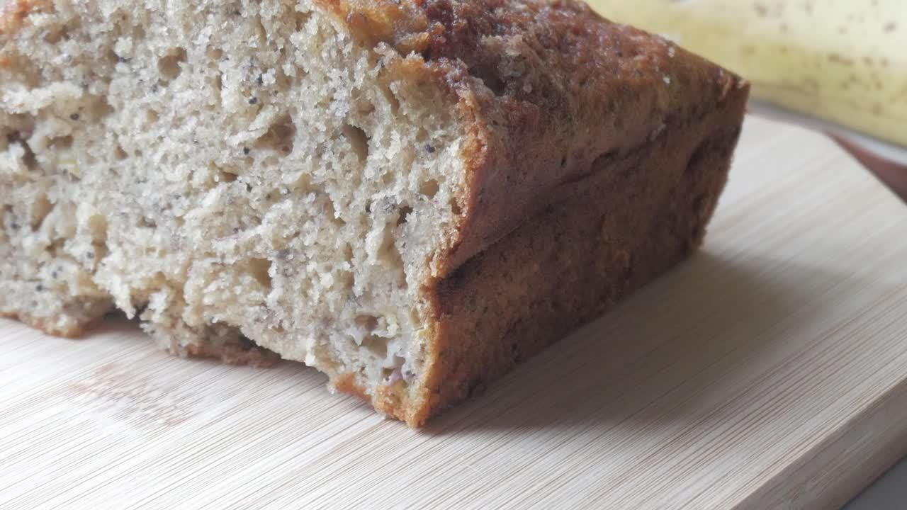 Left pan of banana bread cut in half on a wooden board with a banana in the back.