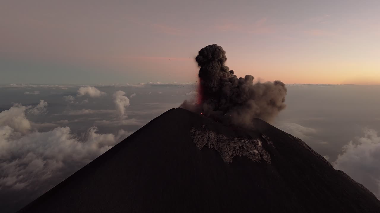 An active volcano emits lava and black smoke, aerial view