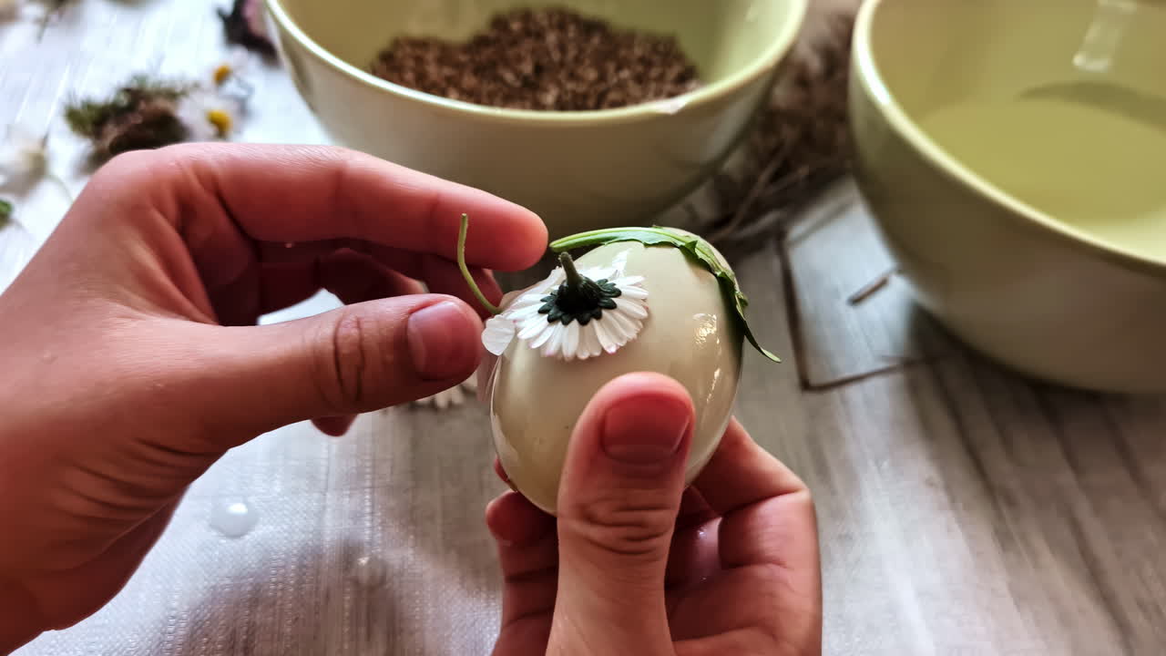 Mani decorano delicatamente un uovo con fiori colorati, creando un design unico e vivace.
