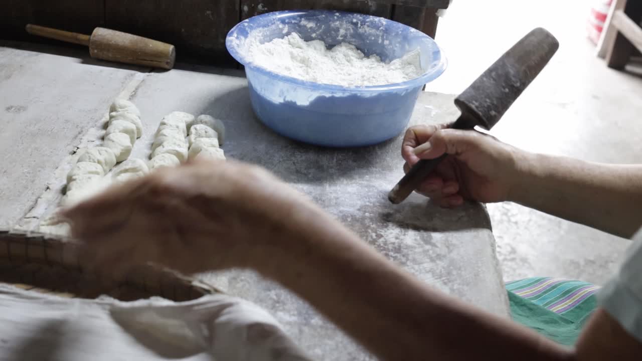 Food vendor rolling uncooked dough into flat round and piercing a hole in each piece using traditional wooden rolling pin while preparing to make clay oven gilled Chinese flat bread or "Huping"