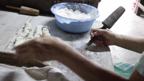 food vendor rolling uncooked dough into flat round and piercing a hole in each piece using traditional wooden rolling pin while preparing to make clay oven gilled chinese flat bread or "huping"