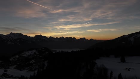 Drone-flies-over-mountains-and-in-the-distance-high-mountains-with-snow-in-Amden,-Weesen,-Glarus,-Switzerland,-sunrise-clouds-in-the-sky