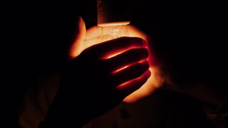 a man holds his hands around an electric light bulb