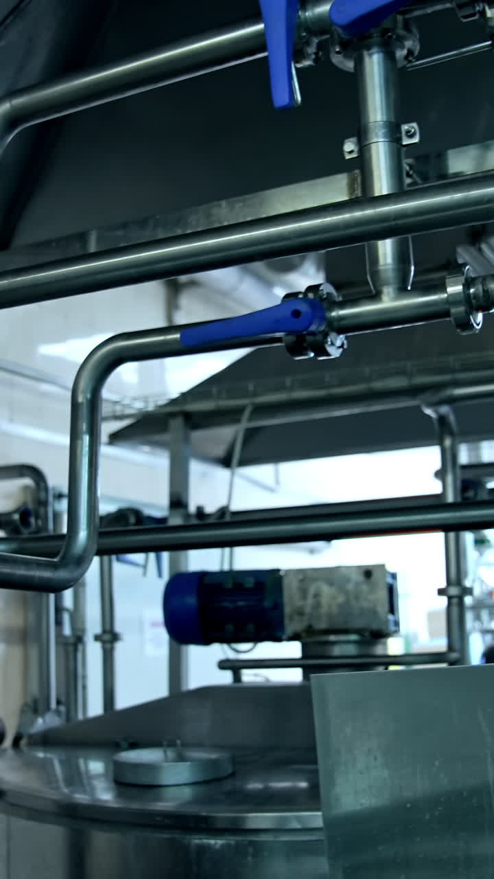 Steel shiny tubes with sensors and valves interlinking with each other. Complicated equipment for dairy food production. Vertical video