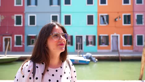 woman with glasses impressed by burano colorful buildings and smiling at camera