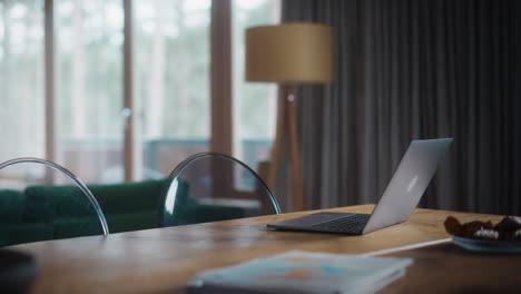 authentic scandinavian home interior in an apartment with laptop computer on a wooden table, trabsparent plastic chairs, big windows and dark curtains. subtle clean minimalistic decor in the flat.