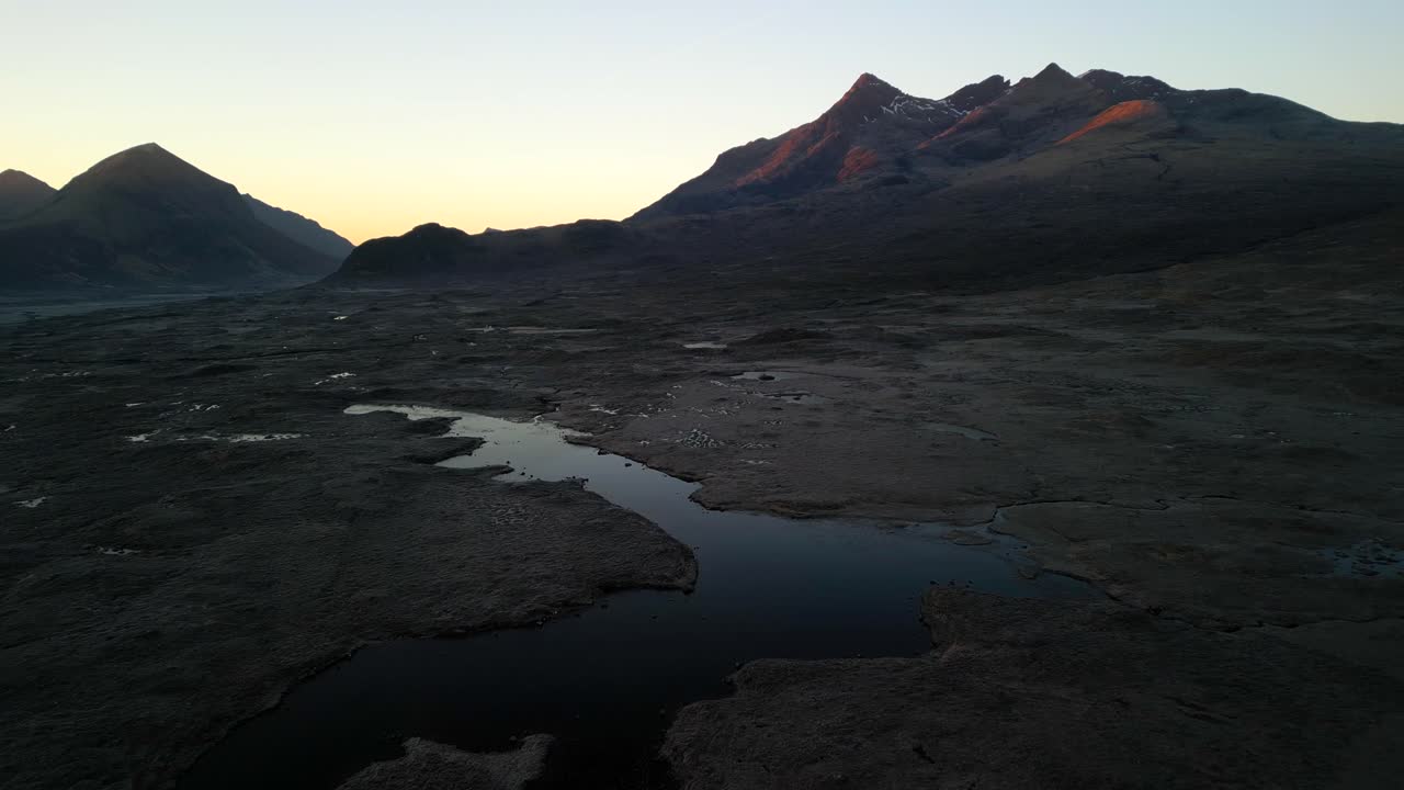 Flyvende over mørk loch ved solopgang mod Black Cuillin-bjergene ved Sligachan på Isle of Skye, Skotland