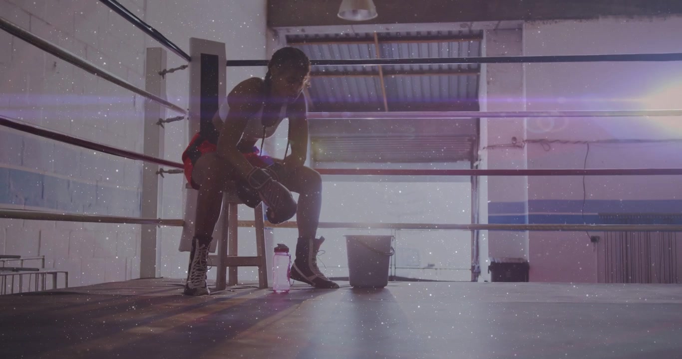 Pugile donna seduta su uno sgabello sul ring, che fa recupero fitness, regolando i guanti e guardando controluce.