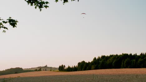 solo paragliding over wide calm yellow fields and forest, pan shot