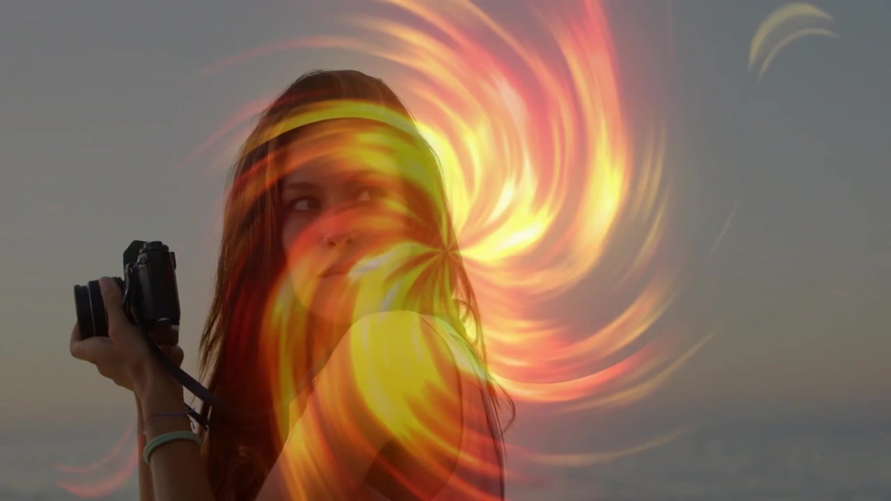 Donna fotografa con fotocamera compatta sulla riva, riprende il tramonto, con un'overlay di fiamme scintillanti che la circonda, sorgendo e svanendo.