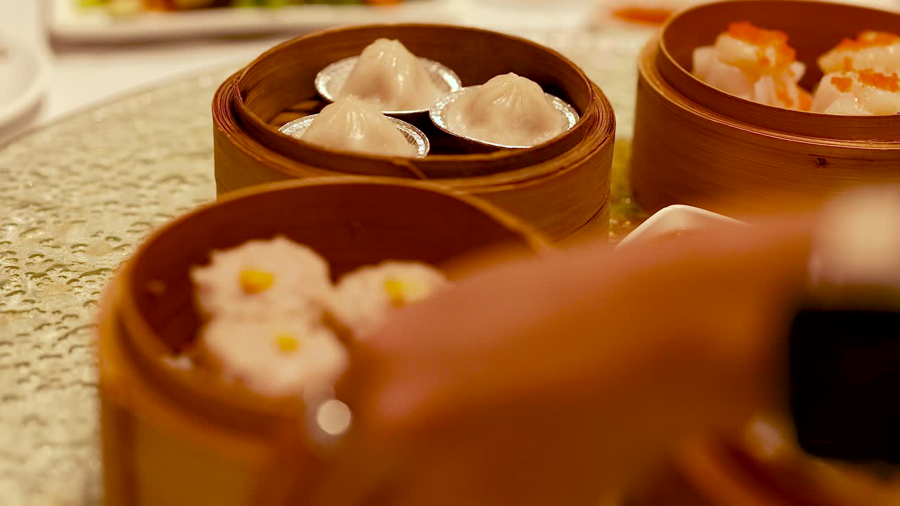 A hand serves dim sum from bamboo steamers in a warmly lit Chinese restaurant, capturing a traditional culinary moment