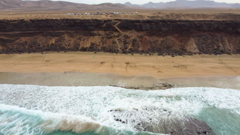 Escalera-Playa-De-Arena-Con-Turistas,-Bañada-Por-El-Mar-Turquesa,-En-El-Fondo-Un-Saliente-Montañoso-Con-Coches-Aparcados