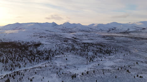 a sweeping cinematic aerial shot of the snowy fish lake and surrounding mountain range near whitehorse, yukon, offering a breathtaking view of the unspoiled northern wilderness of canada.