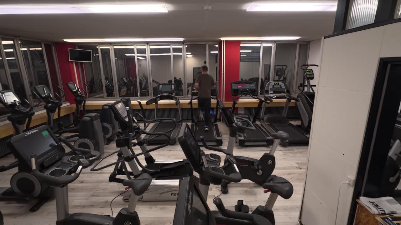 Wide shot of a man exercising alone in a quiet gym, showing solo fitness training, empty workout space, and a calm indoor sports environment with cardio equipment