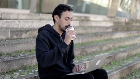 Hombre-Sosteniendo-Un-Vaso-De-Papel-Y-Usando-Una-Computadora-Portátil