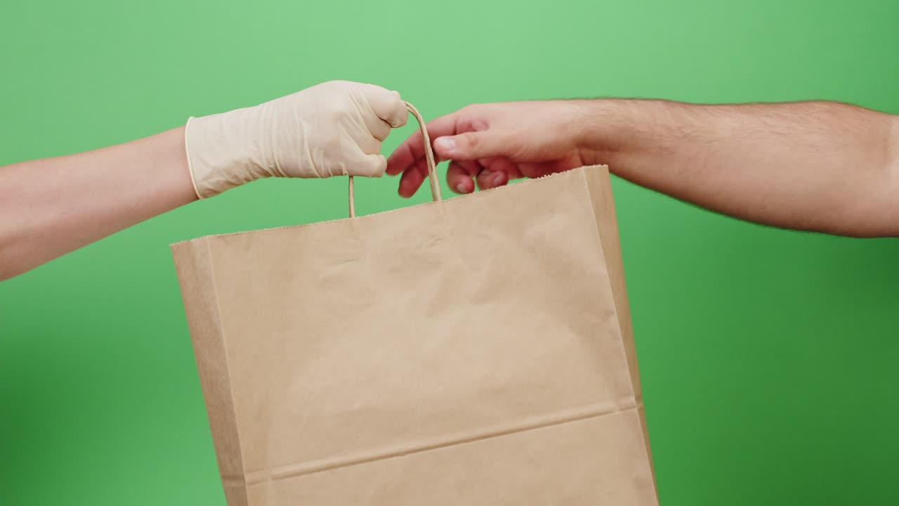 Mano enguantada entregando una bolsa de papel a un cliente en pantalla verde