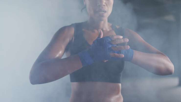 Donna afroamericana che si stringe le fasce da boxe alle mani in un edificio urbano vuoto.