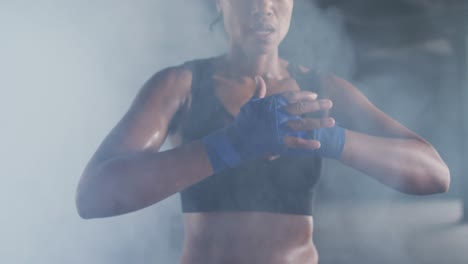 mujer afroamericana apretando la mano de boxeo envuelve en un edificio urbano vacío