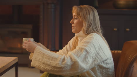 woman at home in lounge with cosy fire with hot drink