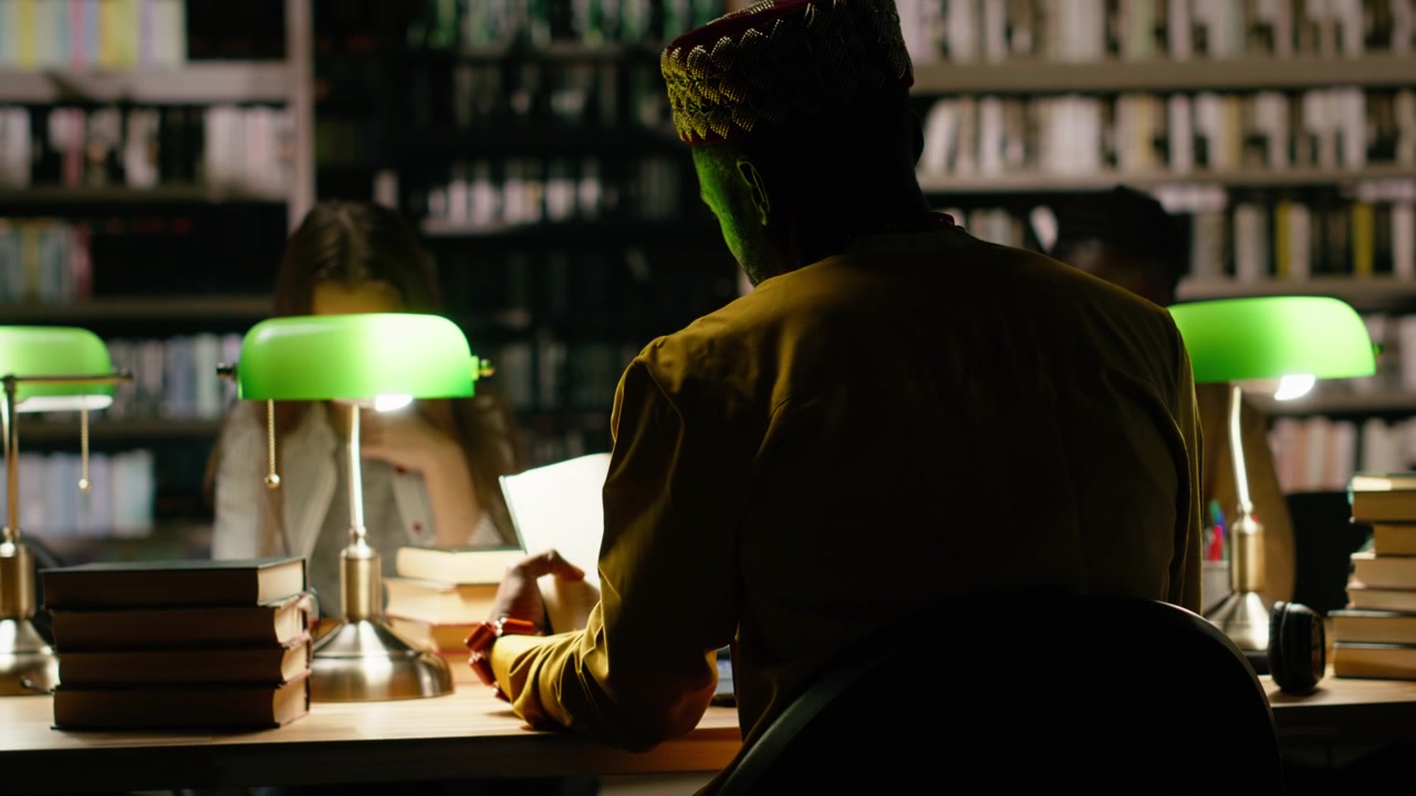 Back view of adult learner in traditional clothes at dark library table