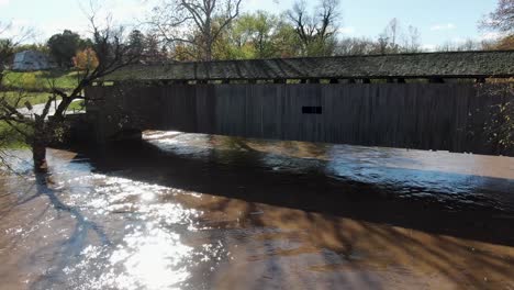 Vista-Aérea-Flotando-Por-Un-Río-Inundado-De-Barro,-Hacia-Un-Largo-Puente-Cubierto-De-Madera