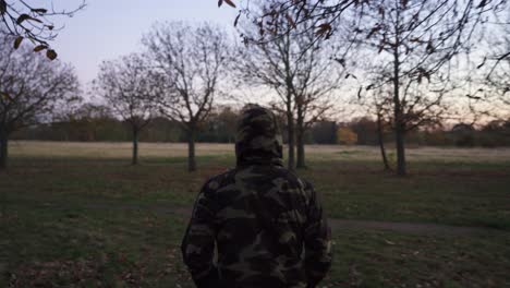 Ich-Folge-Einem-Mann,-Der-An-Einem-Kühlen-Abend-In-Einer-Camouflage-Jacke-Mit-Seinem-Hund-Spazieren-Geht