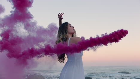 mujer con una bomba de humo rosa bailando en la playa temprano en la mañana celebrando la libertad creativa