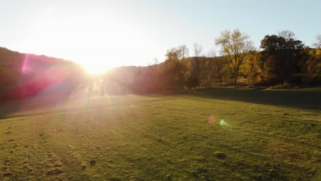 Aerial-epic-drone-shot-of-sun-rays-in-grass-field-surrounded-by-forest-at-sunset-1