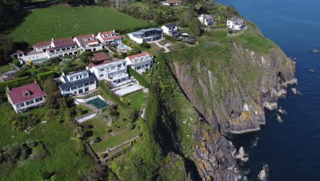 a stunning drone shot slowly curving to the right as it overflies beautiful houses perched at the top of some south devon cliffs