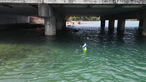 a scuba diver sets up a safety dive float before entering the water under a urban city bridge