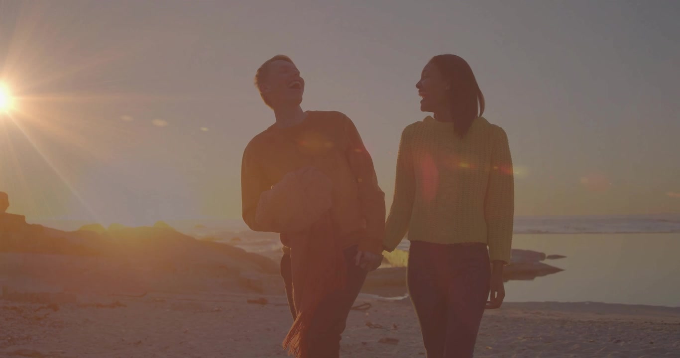 Couple stepping in view and walking rocky beach at sunset for travel content man carrying football