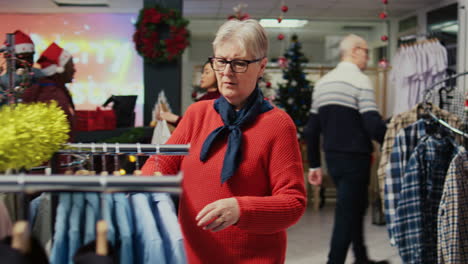 elderly client browsing through clothes in festive xmas ornate shopping mall fashion shop men section, looking for elegant shirt to gift husband for upcoming winter holiday season