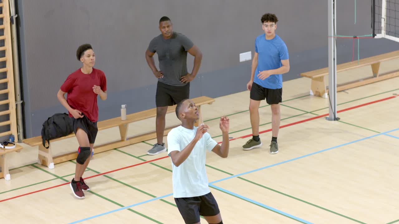 Male team tracking volleyball from right at gym, white tee setter raising performing overhead set