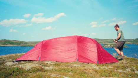 un hombre empacando la tienda después de acampar cerca de la orilla del lago