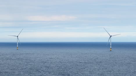 two offshore wind turbines slowly rotate above a tranquil sea under soft daylight, captured in a steady wide shot with a serene, minimalist mood